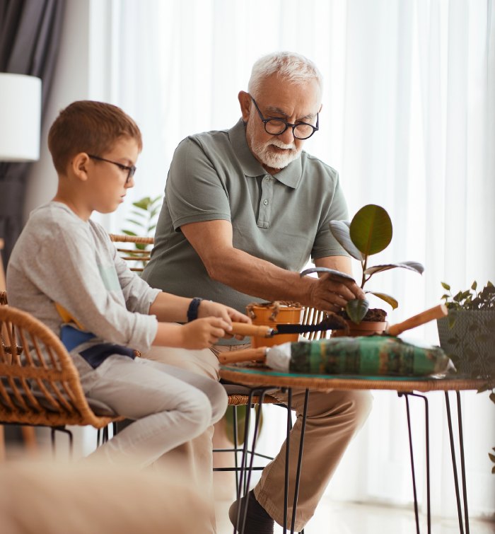 dziadek z wnuczkiem przesadzają kwiatki w salonie